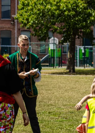 Kinderen in fluohesjes spelen buiten samen met een verklede animator en jeugdwerkers.